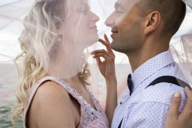 Deniz kenarında yaratıcı hipster düğünü. Gelin pembe bir elbise ve duvak, damat pantolon ve genç bir gömlek giyiyor. Çılgınlık, eğlence ve evliliğe alışılmadık bir yaklaşım.