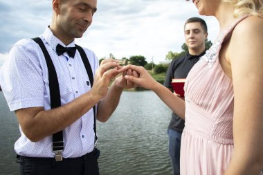 Deniz kenarında yaratıcı hipster düğünü. Gelin pembe bir elbise ve duvak, damat pantolon ve genç bir gömlek giyiyor. Çılgınlık, eğlence ve evliliğe alışılmadık bir yaklaşım.
