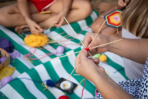 El dokuması mandalalar. Sahilde bir öğretmen öğrencilerine dekoratif desenler örmeyi öğretiyor. Özel sembollerin yaratılması. Eğitim ve el işçiliği kavramı.