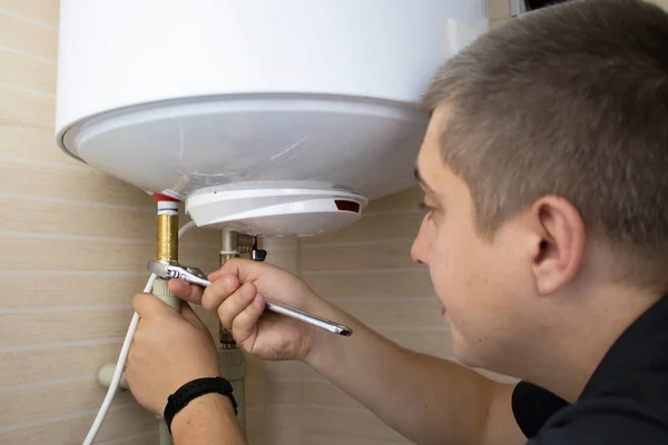 The boiler repair technician uses an adjustable wrench to unscrew or tighten the nut on the pipe. Installing a water heater or dismantling a damaged boiler for later repair.