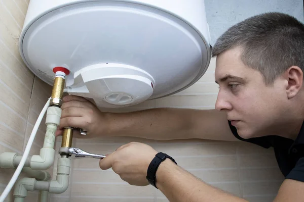 The boiler repair technician uses an adjustable wrench to unscrew or tighten the nut on the pipe. Installing a water heater or dismantling a damaged boiler for later repair.