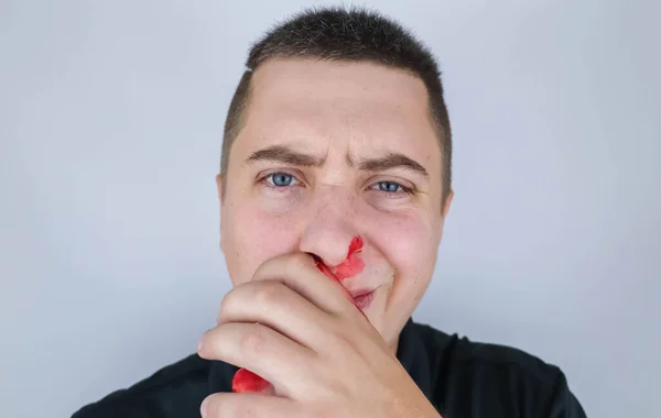 The man has a broken nose after a fight. Blood on hands, cheeks and nose. The consequences of aggressive behavior in men. Attempts to stop the bleeding resulted in blood smearing all over the face.