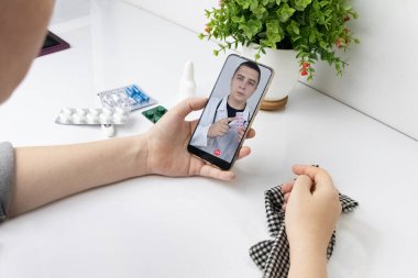 Bir kadın video bağlantısıyla bir doktorla akıllı telefondan iletişim kuruyor. Karantina koşulları altında tıbbi yardım. Uzaktan terapistle görüşme.