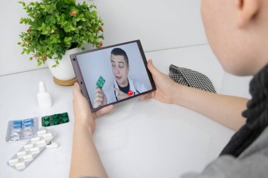 Bir kadın bir tabletle video bağlantısı ile doktorla iletişim kuruyor. Karantina koşulları altında tıbbi yardım. Uzaktan terapistle görüşme.