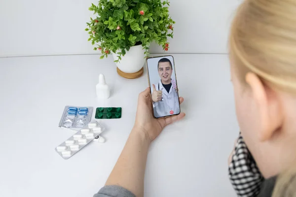 A woman communicates via a smartphone with a doctor via video link. Medical assistance under quarantine conditions. Remote consultation with a therapist