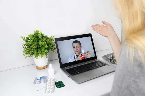 A woman communicates via a computer with a doctor via video link. Medical assistance under quarantine conditions. Remote consultation with a therapist