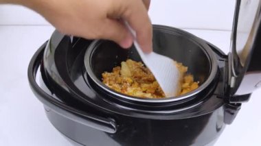 Çoklayıcının makro videosu. Adam tavayı açar ve yemeği karıştırır. Pişmiş yiyeceklerden buhar görülebilir. Mutfakta otomasyon ve kolaylık kavramı..