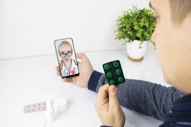 Bir adam video bağlantısıyla bir doktorla akıllı telefon aracılığıyla iletişim kuruyor. Karantina koşulları altında tıbbi yardım. Uzaktan terapistle görüşme.