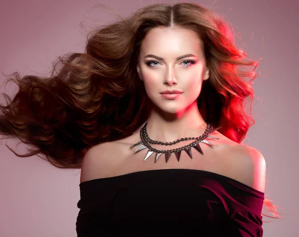 Kadın yüksek moda renkli parlak ışıklar lüks uzun sağlıklı dalgalı, hacimli saç modeliyle. Kolye zincirleri ile güzel kız. Ledy rock'n roll tarzı renkli canlı kırmızı zemin üzerine.