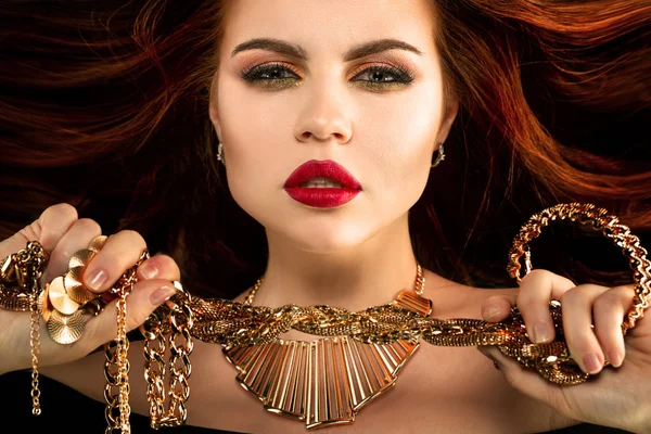 Woman with gold jewelry. Luxurious rich model with necklaces, rings, earrings, bracelets in their hands.