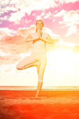 genç güzel ince kadın, güneş doğarken kumsalda yoga uygulamaları. gün batımında Yoga