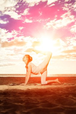 genç güzel ince kadın, güneş doğarken kumsalda yoga uygulamaları. gün batımında Yoga