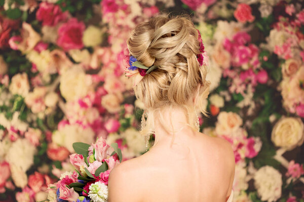 Wedding hairstyle a young girl. Bride. Woman with Flowers in her hair. High stacking, a bundle of curls. Beautiful blonde model. Earrings and bouquet