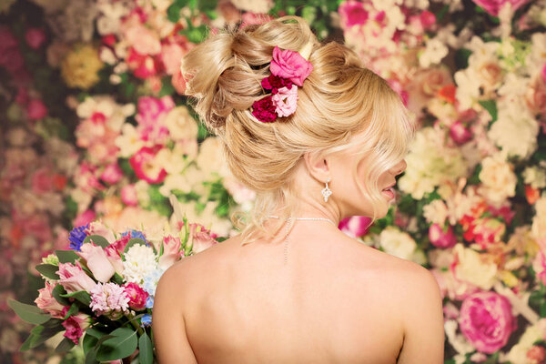 Wedding hairstyle a young girl. Bride. Woman with Flowers in her hair. High stacking, a bundle of curls. Beautiful blonde model. Earrings and bouquet