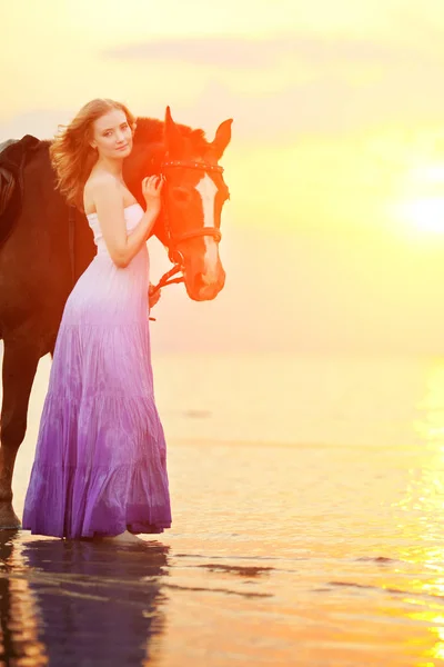 美しい女性のビーチで夕暮れ時の乗馬します 海で太陽の光線で馬との若い美しさの少女 — ストック写真