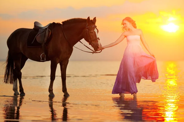 美しい女性のビーチで夕暮れ時の乗馬します 海で太陽の光線で馬との若い美しさの少女 — ストック写真