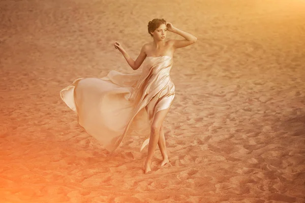 Picture of woman in flying gold cloth in the sand