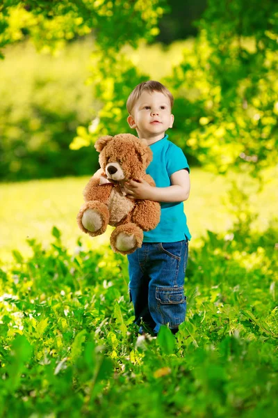 夏の公園を背景におもちゃのクマを持つ小さな男の子 緑の屋外に対してかわいい子供 肯定的な子 夏の風景 — ストック写真