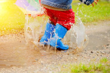 Child jumps on puddles in boots. Baby in the rain. A boy with a rainbow umbrella is walking outside. Autumn, vacation clipart