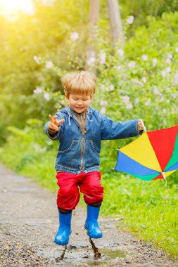 Çocuk boots göletlerde atlar. Yağmur bebek. Bir çocuk bir gökkuşağı şemsiye ile dışarıda yürüyor. Sonbahar, tatil