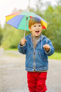 Çocuk boots göletlerde atlar. Yağmur bebek. Bir çocuk bir gökkuşağı şemsiye ile dışarıda yürüyor. Sonbahar, tatil