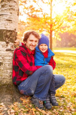 Baba ile oğlu sonbahar parkta yürüyor. Bir çocuk ve bir adam ormanda yürüyüşe eğleniyorlar. Aile doğada zaman harcıyor
