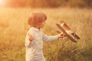 Çocuk pilot pilot uçakta açık havada, karton oyuncak uçak ile yaz gökyüzü artalanda karşı günbatımı, küçük çocuk ile. Retro tonda. seyahat rüyalar