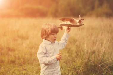 Çocuk pilot pilot uçakta açık havada, karton oyuncak uçak ile yaz gökyüzü artalanda karşı günbatımı, küçük çocuk ile. Retro tonda. seyahat rüyalar