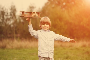 Çocuk pilot pilot uçakta açık havada, karton oyuncak uçak ile yaz gökyüzü artalanda karşı günbatımı, küçük çocuk ile. Retro tonda. seyahat rüyalar