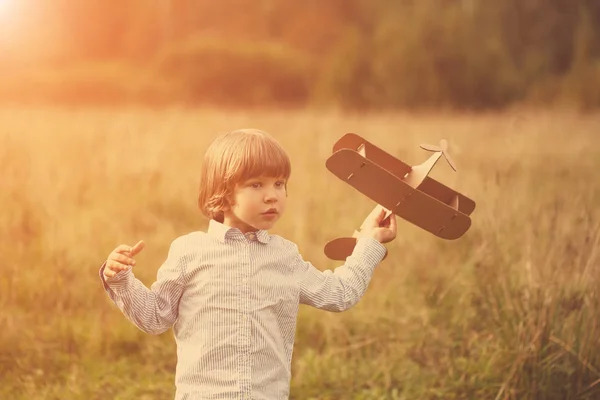 子夏空の背景にダン ボール飛行機を屋外で遊んで 日没の少年で飛行機とパイロットのアビエイター レトロなトーンします 旅の夢 — ストック写真