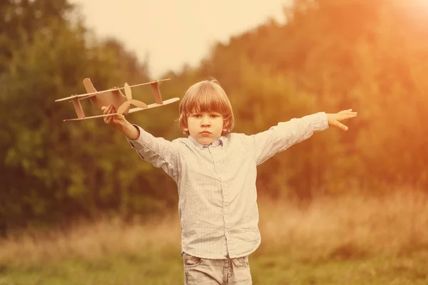 子夏空の背景にダン ボール飛行機を屋外で遊んで 日没の少年で飛行機とパイロットのアビエイター レトロなトーンします 旅の夢 — ストック写真