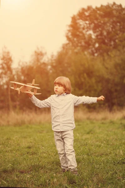 Çocuk pilot pilot uçakta açık havada, karton oyuncak uçak ile yaz gökyüzü artalanda karşı günbatımı, küçük çocuk ile. Retro tonda. seyahat rüyalar