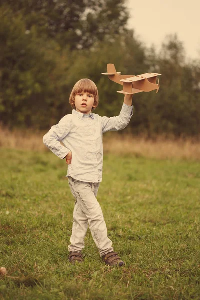 Çocuk pilot pilot uçakta açık havada, karton oyuncak uçak ile yaz gökyüzü artalanda karşı günbatımı, küçük çocuk ile. Retro tonda. seyahat rüyalar