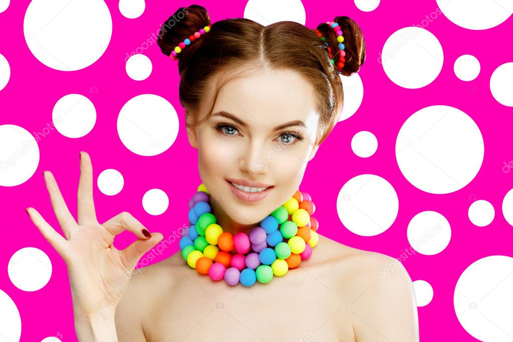 A bright girl model shows okay hand, fingers. Beautiful, stylish, young woman in a candy doll style with massive beads around her neck