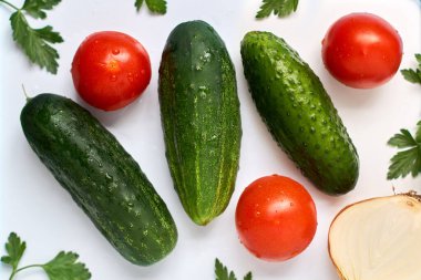 Üç salatalık, üç domates, yarım soğan ve beyaz zemin üzerinde su damlaları olan maydanoz..