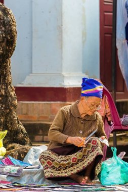 Luang Prabang, Laos - 11 Ocak 2017: Yaşlı bir kadın kumaş üzerine bir şehir sokak satıyor. Metin için yer kopyalayın. Dikey