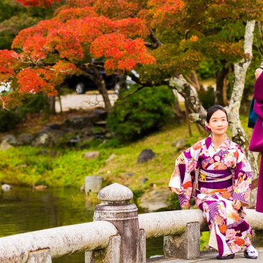 Kyoto, Japonya - 7 Kasım 2017: Bir kız bir kimono içinde bir köprü üzerinde oturuyor. Metin için yer kopyalayın