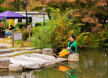 Kyoto, Japonya - 7 Kasım 2017: Bir taş bir fotoğrafçısına poz bir su birikintisi yakın bir kız. Metin için yer kopyalayın
