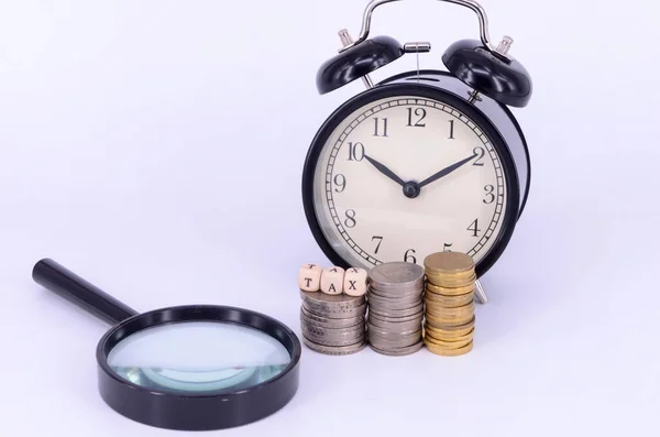 目覚まし時計と虫眼鏡のついたコインに白い背景で書かれた Tax という言葉は 税時間の概念です 選択的焦点 — ストック写真