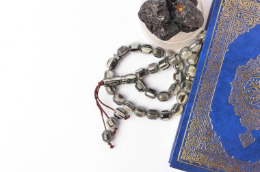 Kur 'an' ın en üstteki görüntüsü, beyaz arka planda tespih ve kuru tarihler. Aylık oruç kültürü Müslümanlar ve tanrıya dua, Ramadhan yemeği sembolik doğu Arapça.