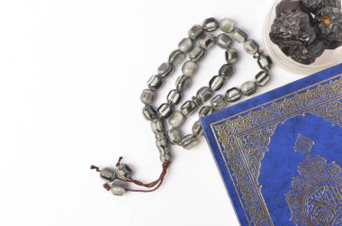 Kur 'an' ın en üstteki görüntüsü, beyaz arka planda tespih ve kuru tarihler. Aylık oruç kültürü Müslümanlar ve tanrıya dua, Ramadhan yemeği sembolik doğu Arapça.