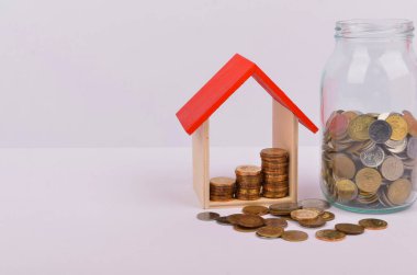 Konut kredisi almak için para biriktirmek hayat amacı için para biriktirmek. Beyaz arka planda bozuk paraları olan tahta bir oyuncak ev. Seçici odak.