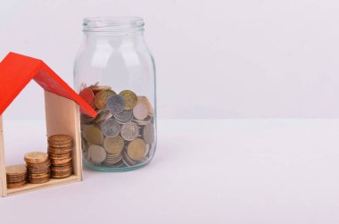 Konut kredisi almak için para biriktirmek hayat amacı için para biriktirmek. Beyaz arka planda bozuk paraları olan tahta bir oyuncak ev. Seçici odak.