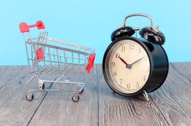 Alışveriş arabası ve ahşap yüzeyde klasik çalar saat. Satış zamanı alışveriş merkezi market tüketicisi konsepti satın al. Seçici odak.