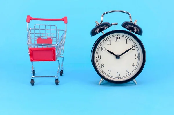 青の背景にショッピングカートと古典的な目覚まし時計 時間市場店消費者の概念を販売しなさい 選択的焦点 — ストック写真