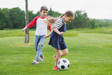 happy little children playing soccer on meadow with green grass clipart