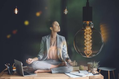 light bulb representing creative thinking and young businesswoman meditating in lotus position on work table clipart