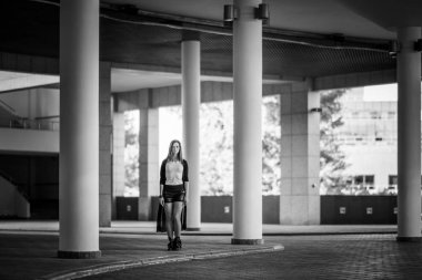 Güzel Rus kız parkta uzun boylu beyaz sütunlar arasında duruyor. Siyah şort, Beyaz mayoyu ve siyah bir hırka giyiyor. Siyah beyaz fotoğraf