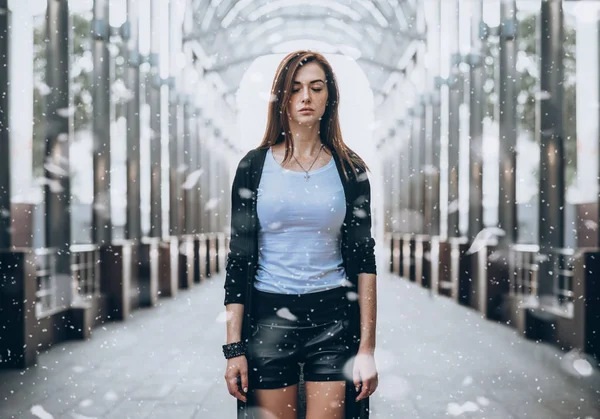 Uma menina fica no meio de uma colunata da cidade na queda de neve. Triste retrato de uma jovem . — Fotografia de Stock