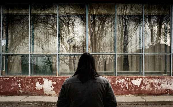 A man with long hair stands in front of a ruined building with his back to the camera. Homecoming. — Stock Photo, Image